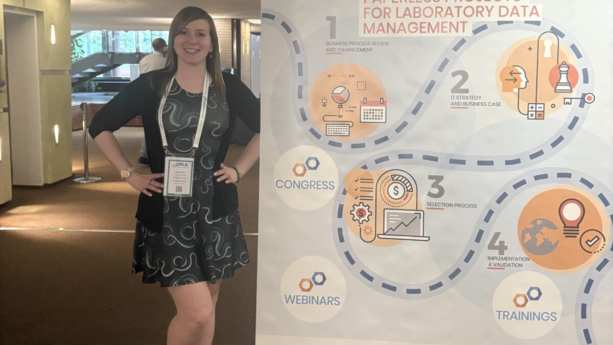 Photograph of Dr Samantha Pearman-Kanza standing by the Paperless Labs Academy Conference Banner